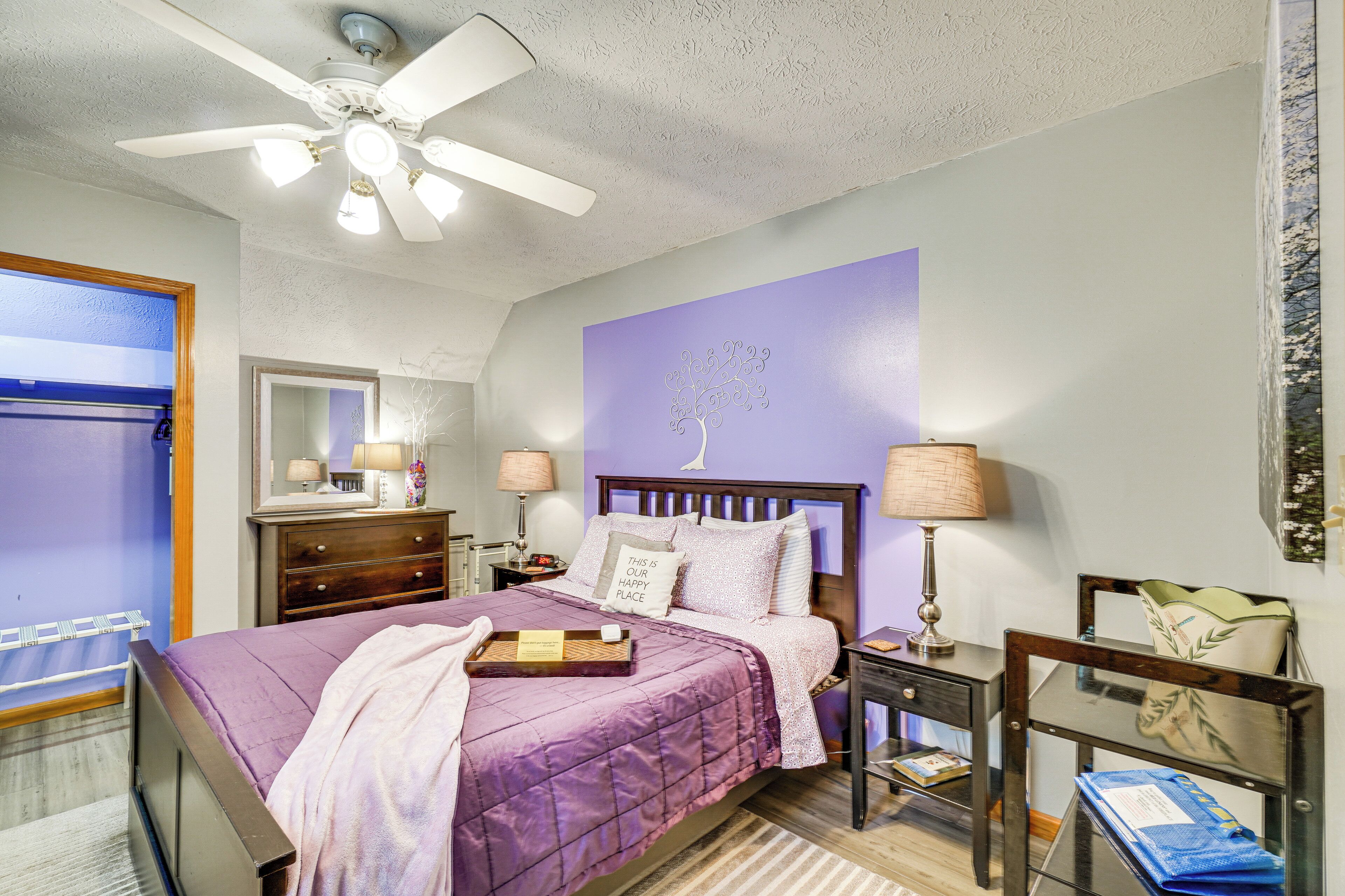 Ein Schlafzimmer mit violettem Bettbezug, Deckenventilator, Nachttisch mit Lampe und einem Ankleidezimmer.