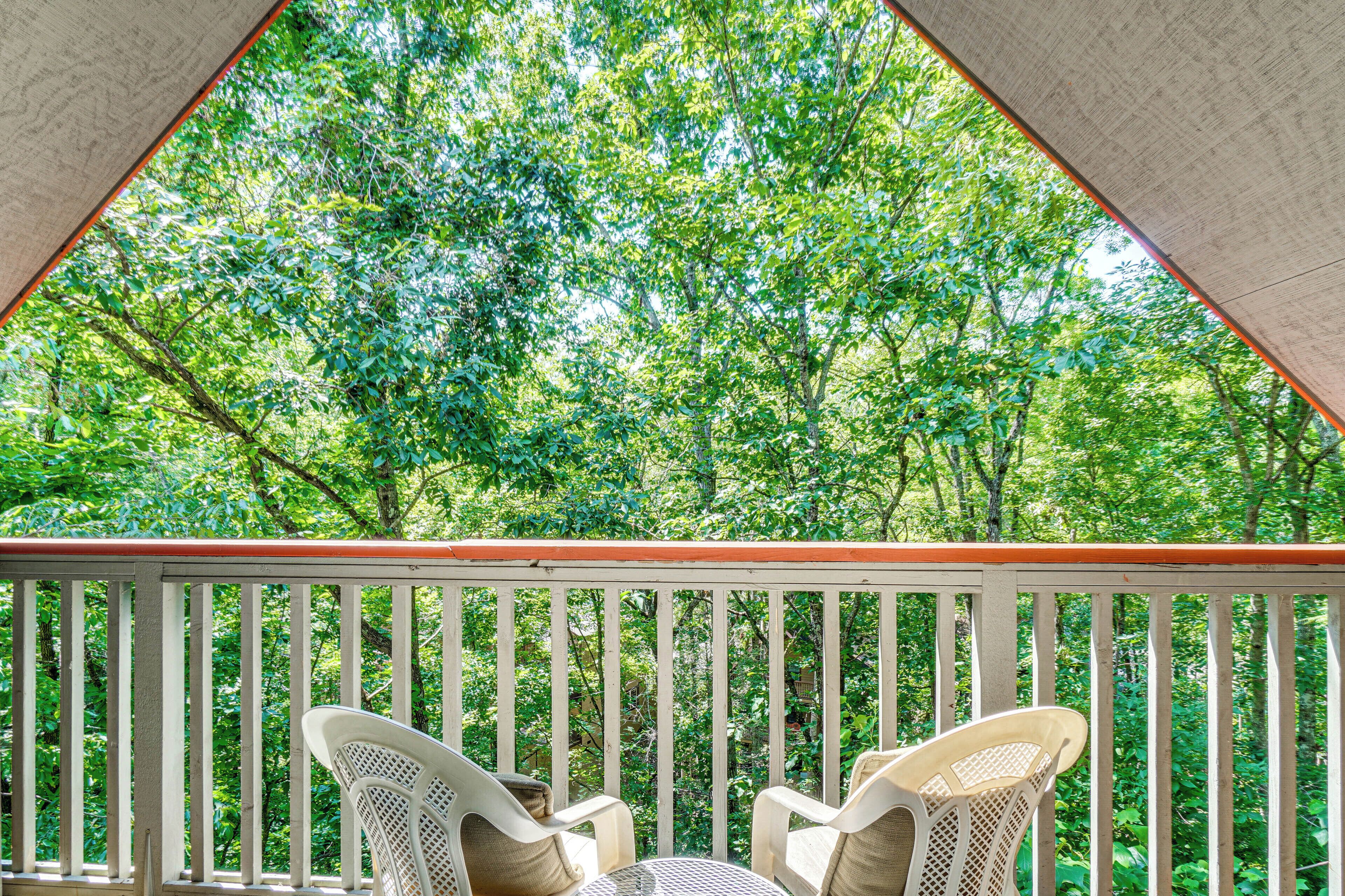 A balcony with white railings and wicker chairs, overlooking a dense green forest.
