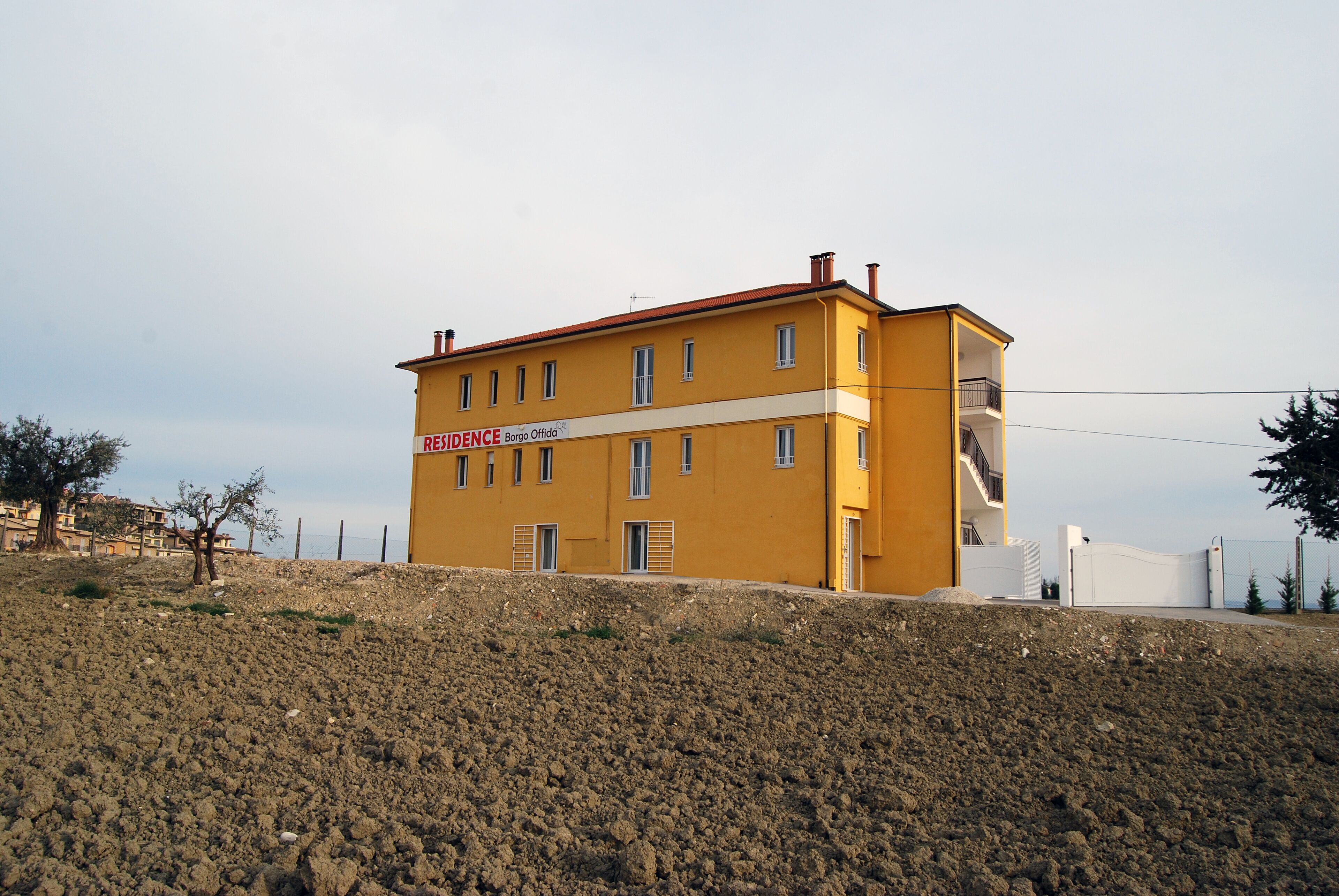 A yellow building with a red roof, labeled "RESIDENCE BORGIO Officina." It has multiple windows and a staircase leading to an upper floor.