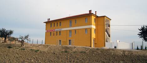 A yellow building with a red roof, labeled "RESIDENCE BORGIO Officina." It has multiple windows and a staircase leading to an upper floor.