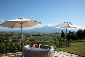 A hot tub with two umbrellas, a scenic vineyard view, and a mountainous backdrop.