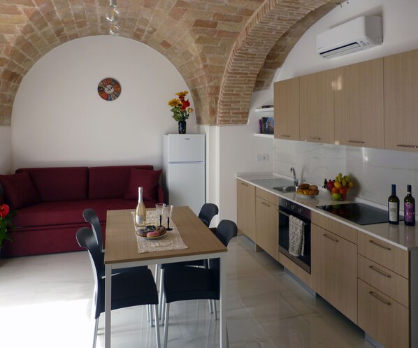 Una cocina moderna con comedor, que presenta un arco de ladrillo, un refrigerador, armarios de madera y un sofá rojo.