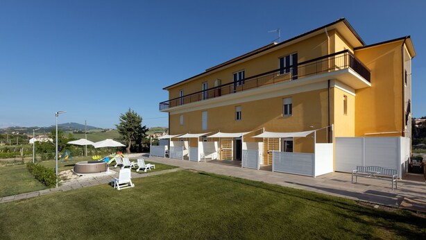 A yellow building with a balcony, outdoor seating, and a grassy area.