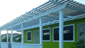 A beach house with a covered porch, a small deck, and a green and white exterior. - Sagusta Gardens Cosy Apartment 2 (Whitby)