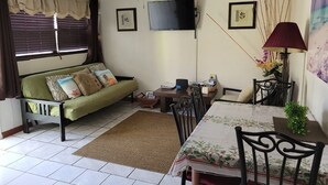 A living room with a sofa, dining table, chairs, a ceiling fan, a TV, and framed pictures on the wall. - Sagusta Gardens Cosy Apartment 2 (Whitby)