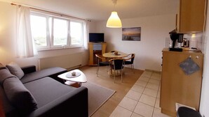 Un espace de vie compact comprenant un canapé, une petite table à manger, un téléviseur et un coin cuisine.