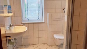 Une salle de bain avec un lavabo blanc, des toilettes et une fenêtre.