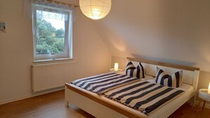 Une chambre à coucher avec un lit, une fenêtre donnant sur un espace verdoyant, un radiateur et un luminaire suspendu.