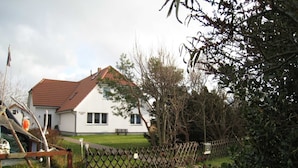 Une maison blanche avec un toit rouge, une cour clôturée et un banc.