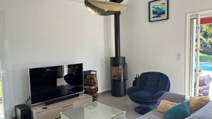 Un salon moderne avec un téléviseur, un canapé, une table basse en verre et un poêle à bois.