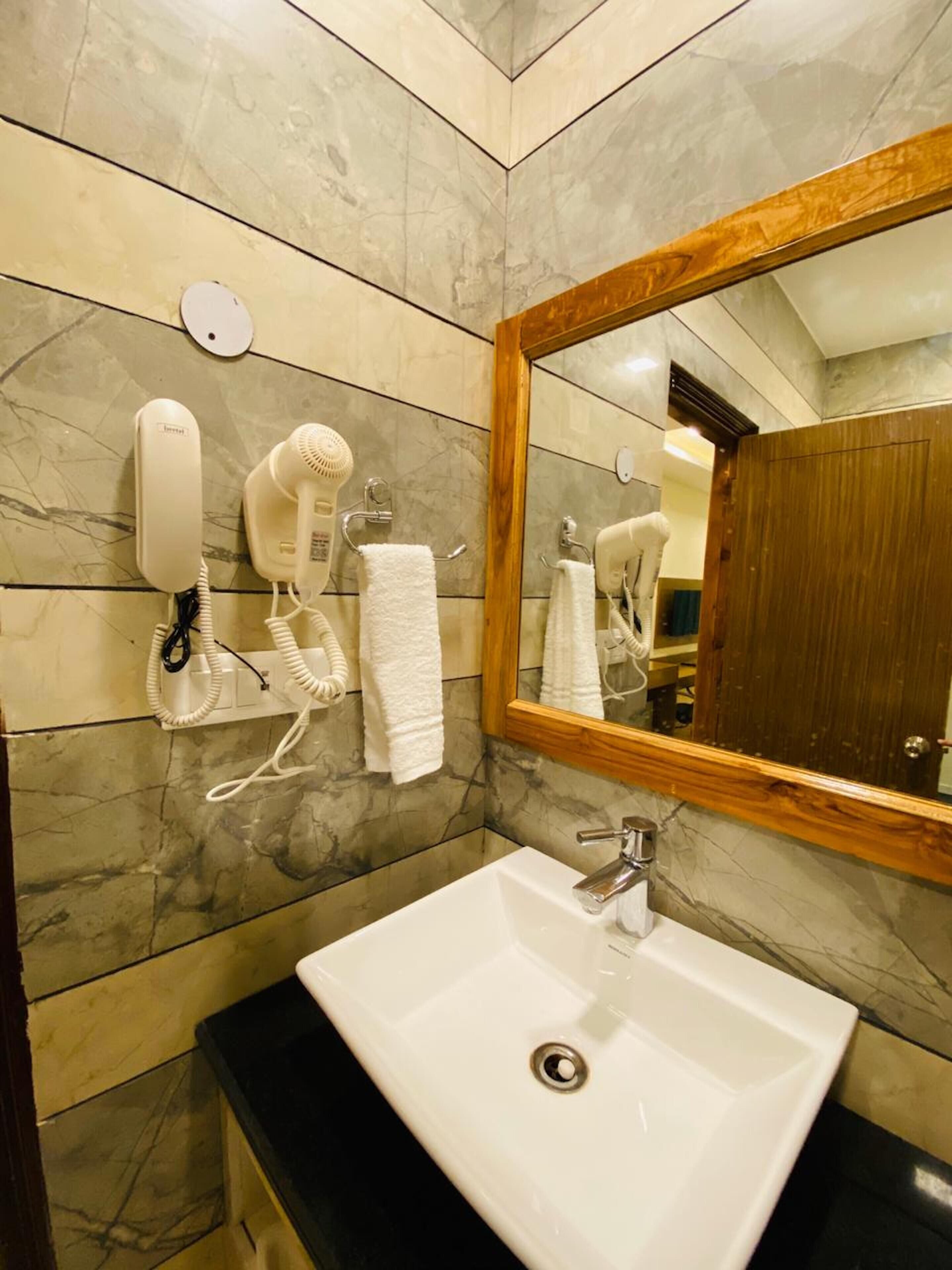 A bathroom with a marble wall, a white sink, a mirror, and two hair dryers mounted on the wall.