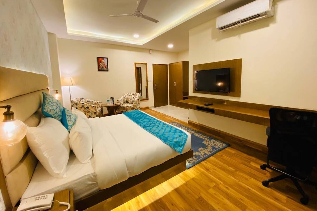 Habitación de hotel con cama, escritorio, silla, televisor y aire acondicionado.