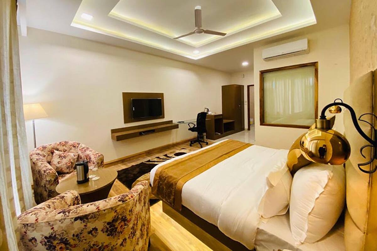 Habitación de hotel con cama, escritorio, silla, televisor y ventilador de techo.