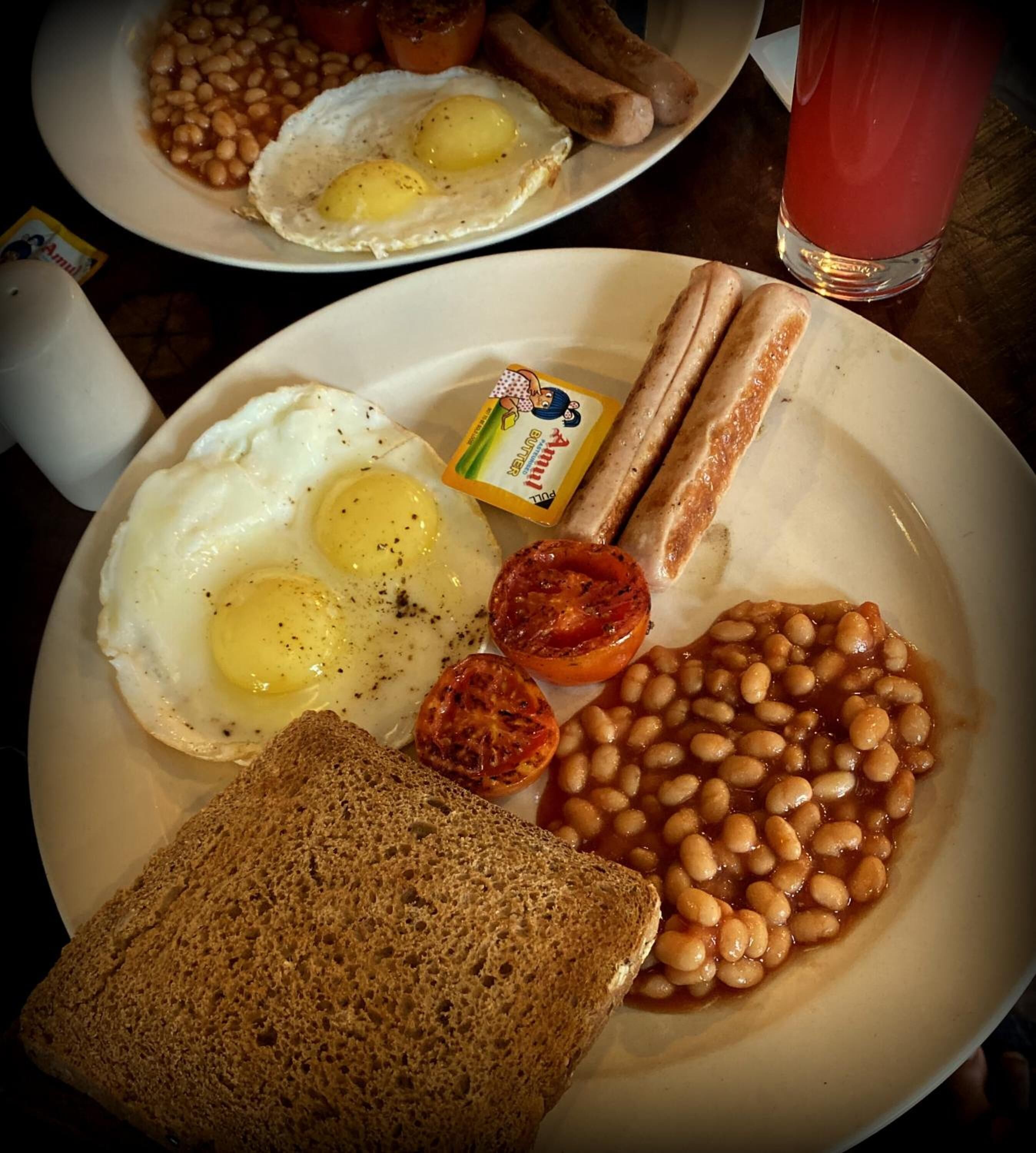 A breakfast plate with eggs, beans, bacon, a slice of toast, and a glass of juice.