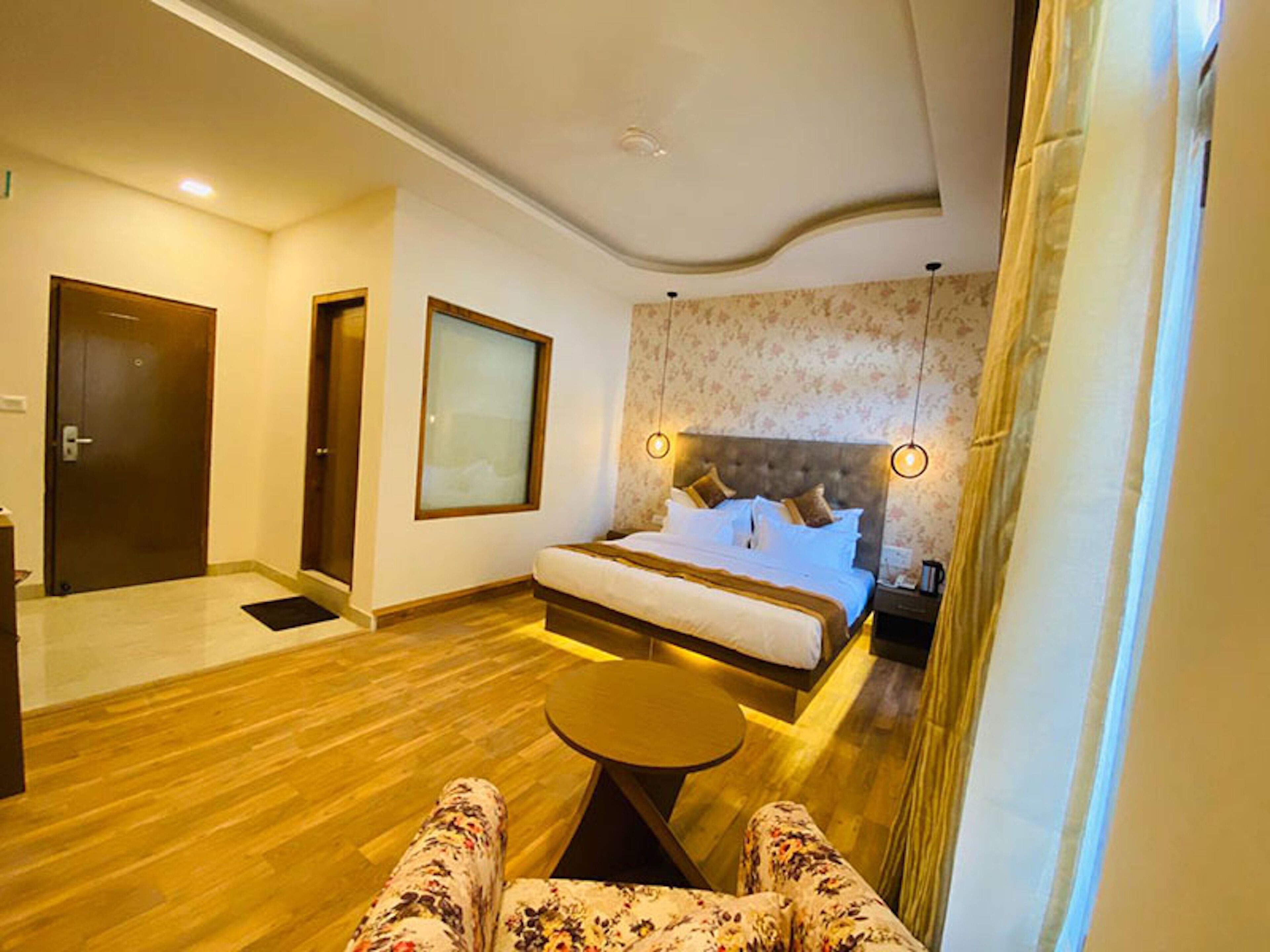 A hotel room with a large bed, a small round table, and a view of the hallway.