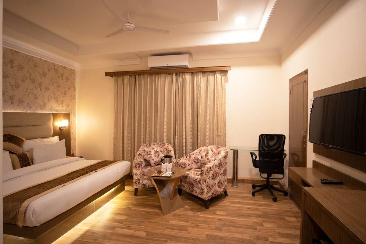 Habitación de hotel con una cama, dos sillones con motivos florales, un escritorio con televisor y un ventilador de techo.
