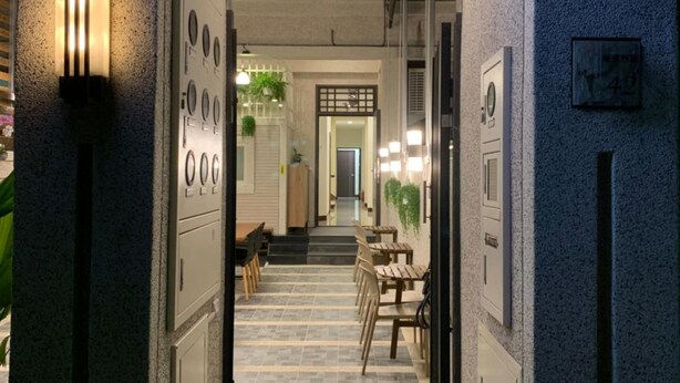 A hallway with a digital clock displaying 9:40, leading to a seating area with tables and chairs. - 910 Hostel (Yuli)