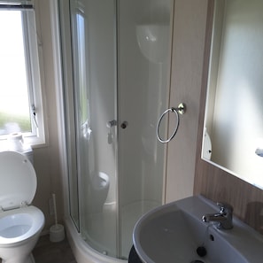 A modern bathroom with a glass shower enclosure, a white toilet, and a sink with a mirror above it. - Camber Sands Lodge (Rye)