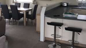 Cocina compacta con comedor, que incluye una mesa y sillas, una pequeña barra con taburetes y un ventanal con cortinas.