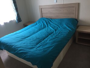 A single bed with a wooden headboard, a bedside table, and a nightstand. - Camber Sands Lodge (Rye)