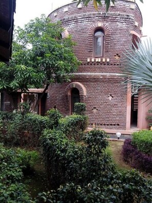 A brick building with a circular structure, arched windows, and a small door. - Hotel Shyam Farm House and Resort (Talala)