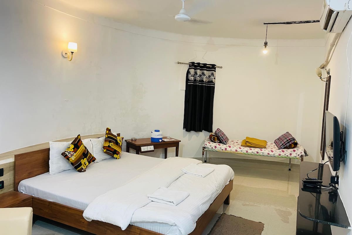 A neatly arranged hotel room with a wooden bed, a bedside table, a small desk, a television, and a ceiling fan.