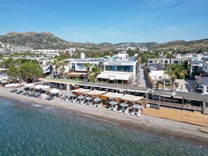 A coastal hotel with a beachside location, including sun loungers and umbrellas, and a view of the sea and hills in the background. - Acropol Of Bodrum Beach Hotel (Bodrum)