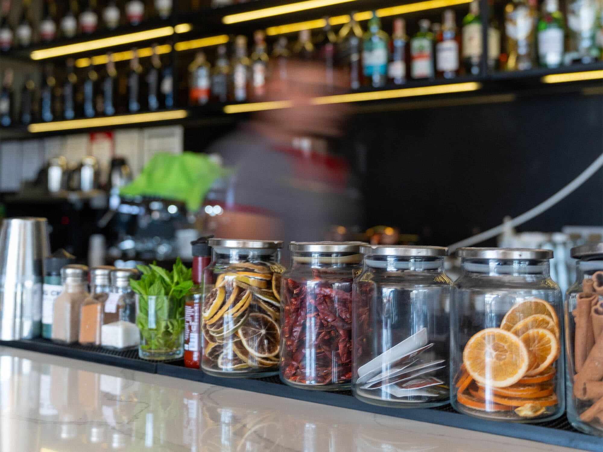 Un bar avec des étagères remplies de bouteilles et de bocaux contenant des fruits et des herbes séchées.