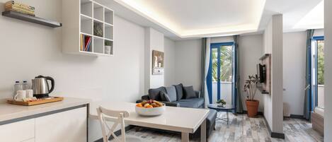 A modern living room with a sofa, a dining table, a kitchen area, and a large window.