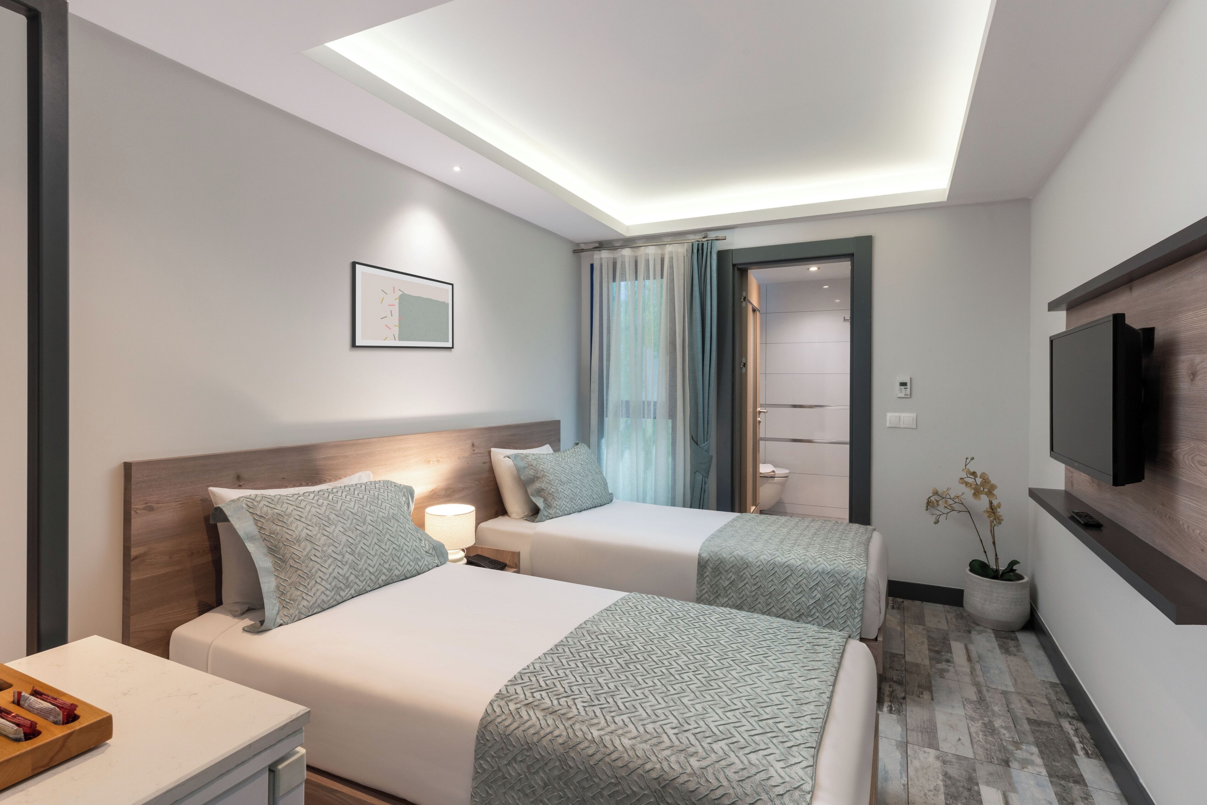 A hotel room with two beds, a TV, a ceiling light, and a bathroom visible through an open door.