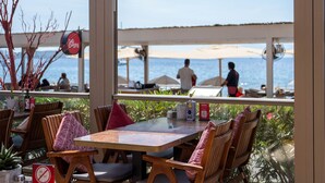 Café al aire libre con mesas y sillas de madera, vista al mar y un cartel que indica prohibido fumar.