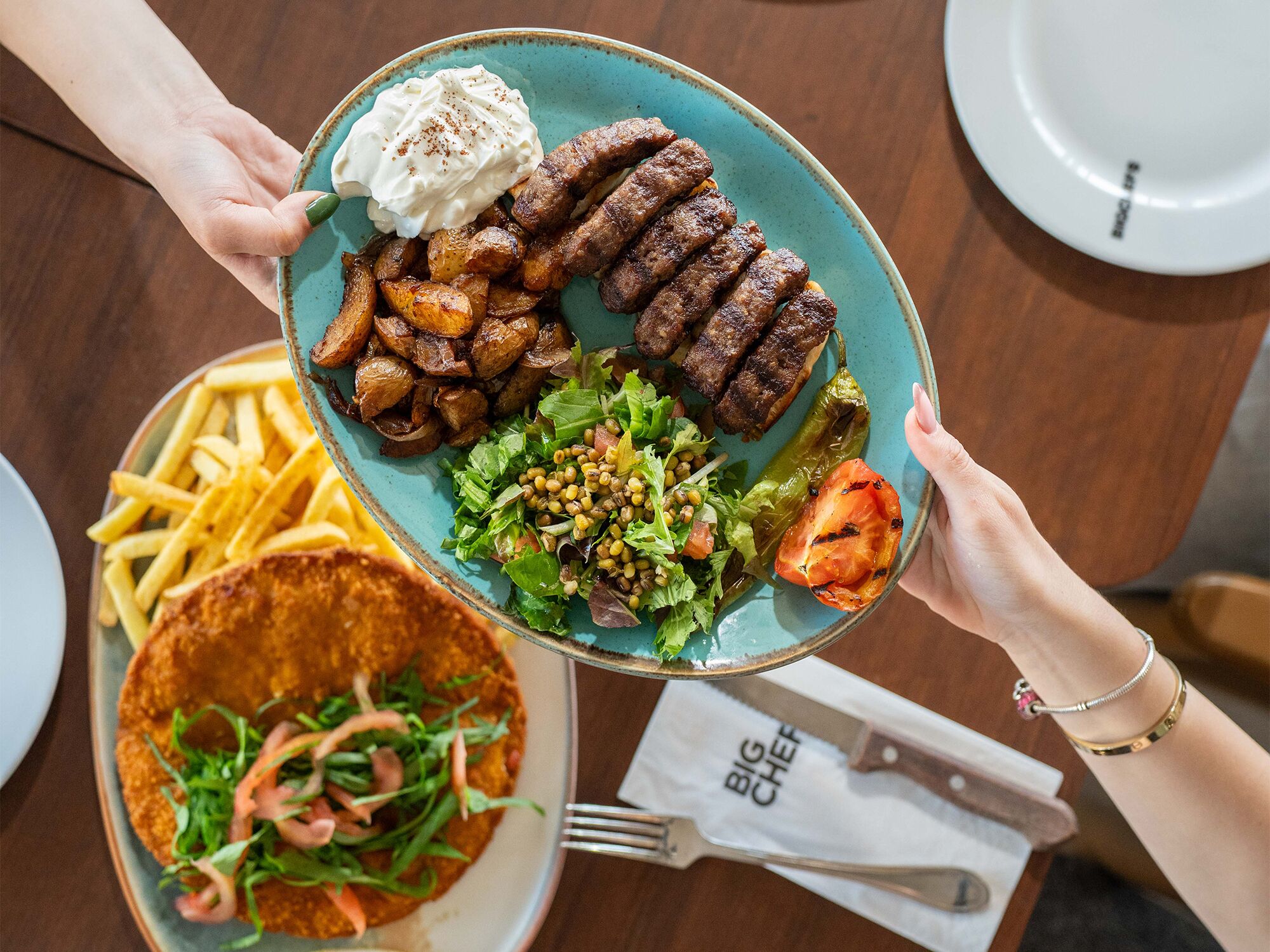 Een persoon houdt een bord vast met eten, waaronder friet, vlees en een salade.