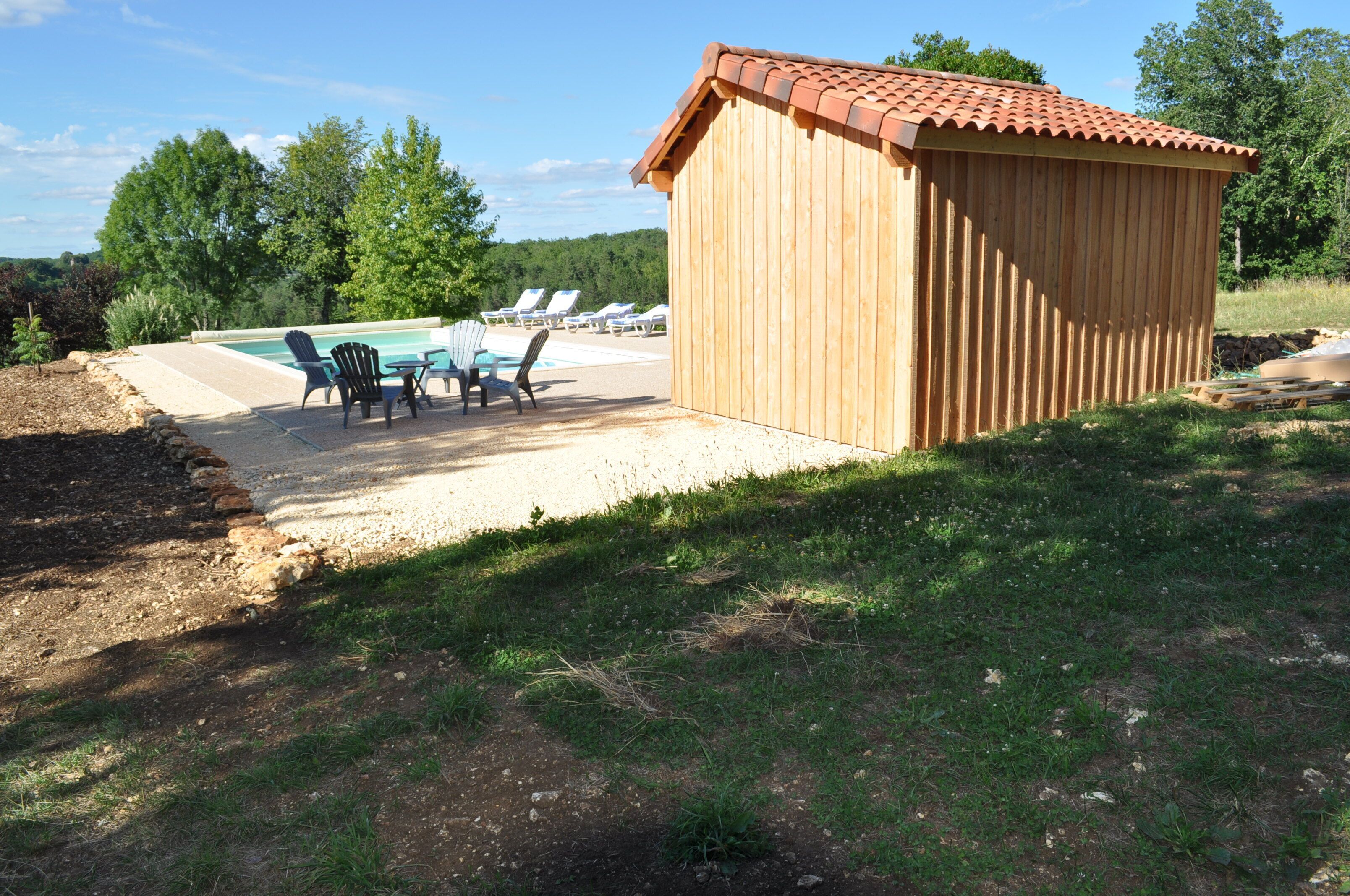 A wooden shed with a tiled roof, a pool with lounge chairs, and a grassy area.