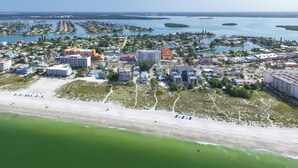 Vista aérea de un pueblo costero con playa, puerto deportivo y diversos edificios, incluyendo hoteles y zonas residenciales.