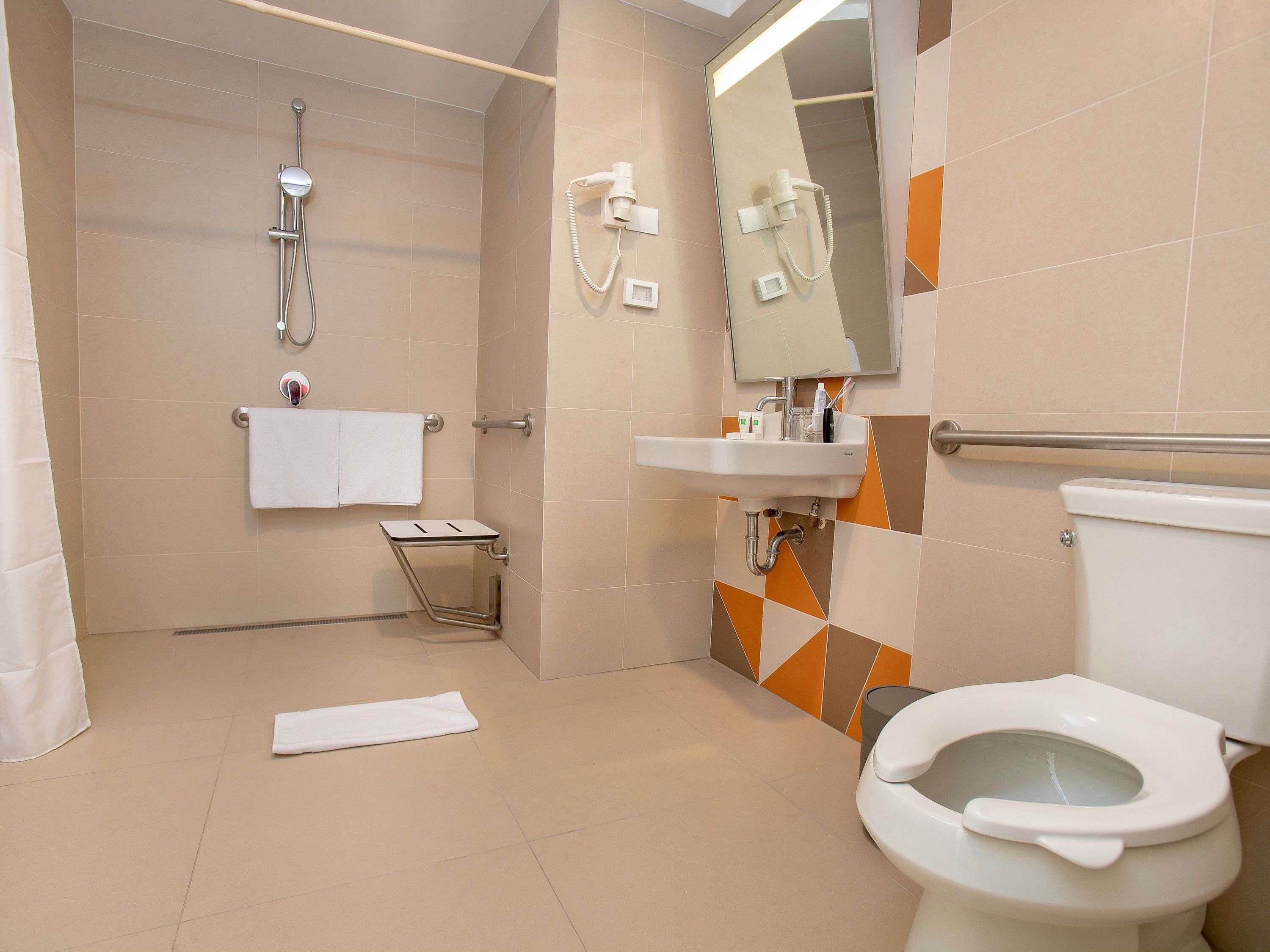 Un baño moderno con ducha, inodoro, lavabo y un pequeño taburete.