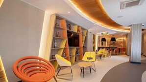 A modern interior with a curved ceiling, built-in bookshelves, and a seating area with orange chairs. - ibis Styles Lima Benavides Miraflores Hotel (Lima)