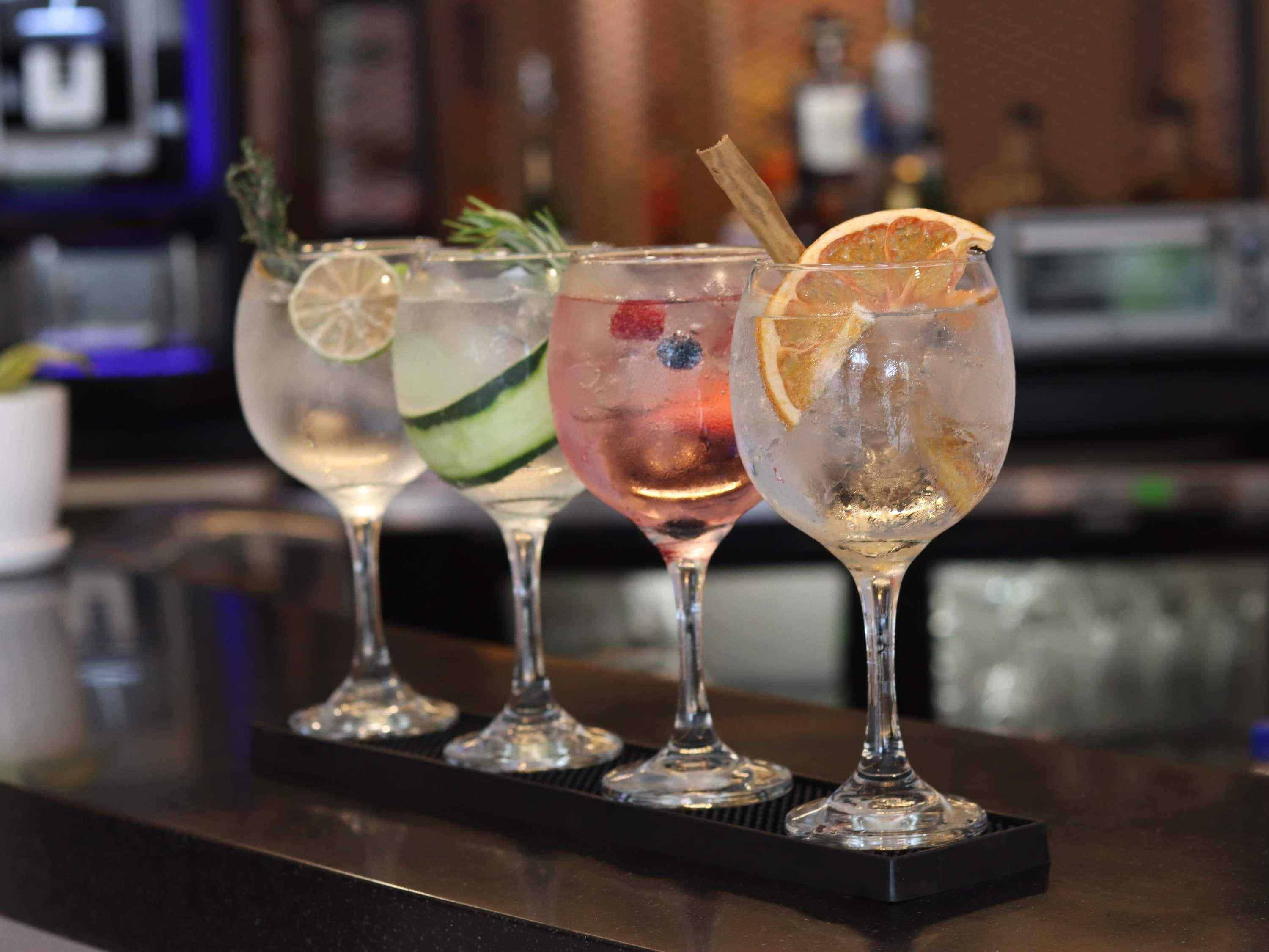 Four glasses of cocktails with garnishes on a bar counter.
