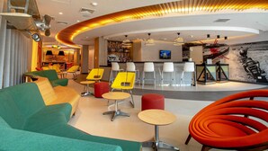 A modern lobby with a curved ceiling, seating areas, a bar, and a wall-mounted TV. - ibis Styles Lima Benavides Miraflores Hotel (Lima)