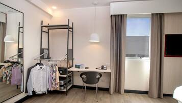 A hotel room with a bed, a desk, a chair, a wardrobe, a mirror, and a window with curtains.