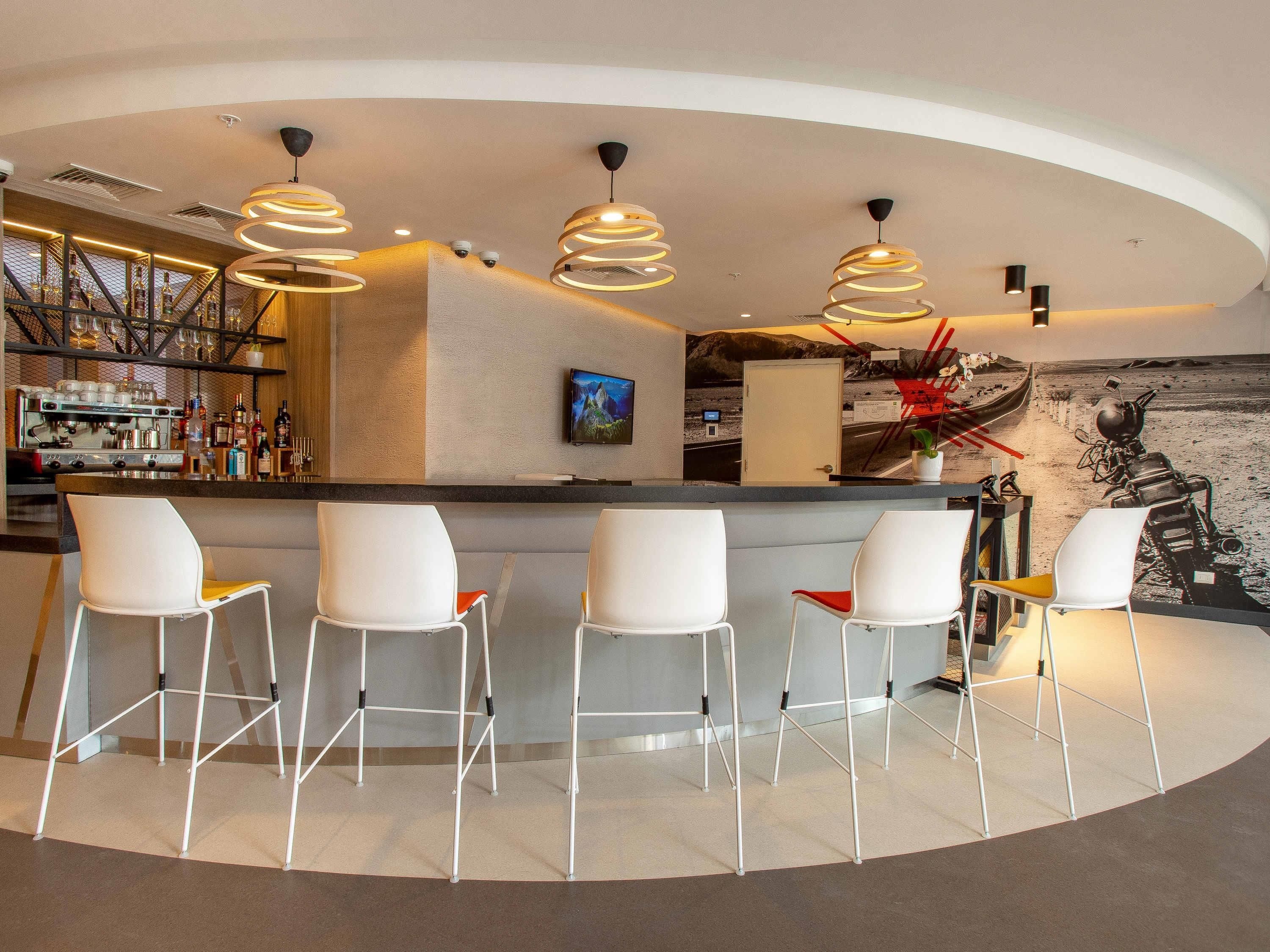 Zona de bar moderna con una barra curva, taburetes blancos e iluminación colgante.
