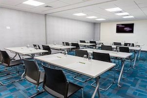 Una sala de conferencias con mesas, sillas y una pantalla de televisión.