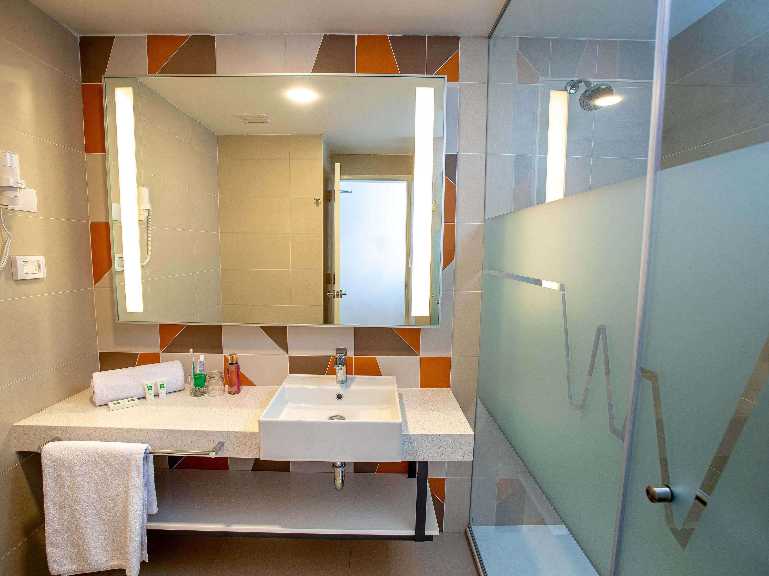Un baño moderno con tocador de doble lavabo, un espejo grande y cabina de ducha con mampara de vidrio.
