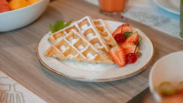 A plate with waffles, strawberries, and cherries, with a glass of orange juice in the background.
