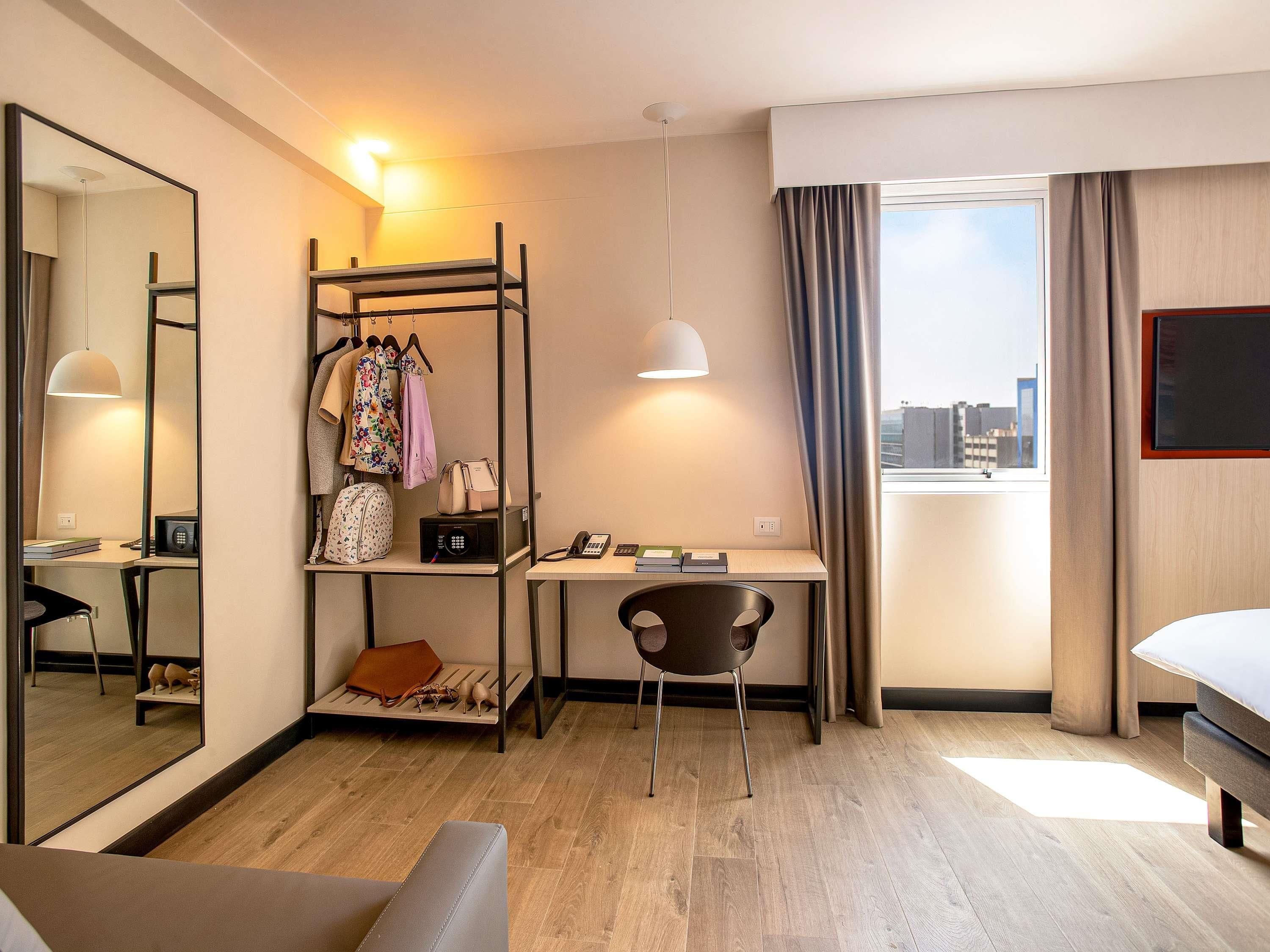 Habitación de hotel con escritorio, silla, cama, armario y un espejo grande.