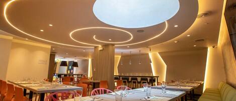 A modern dining area with multiple tables, chairs, and a central light fixture.