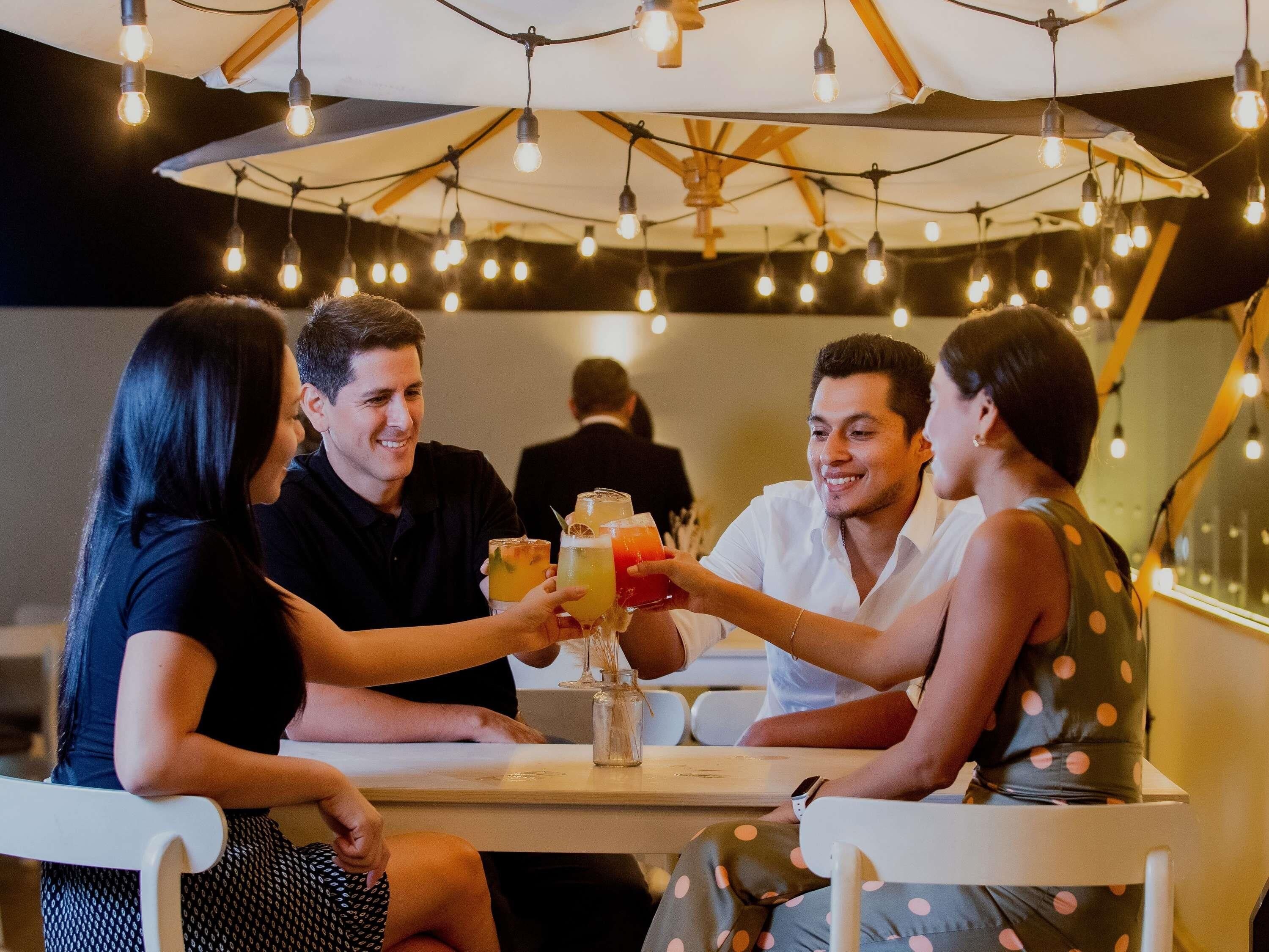 Un grupo de personas sentadas en una mesa al aire libre con luces colgantes y un paraguas grande.