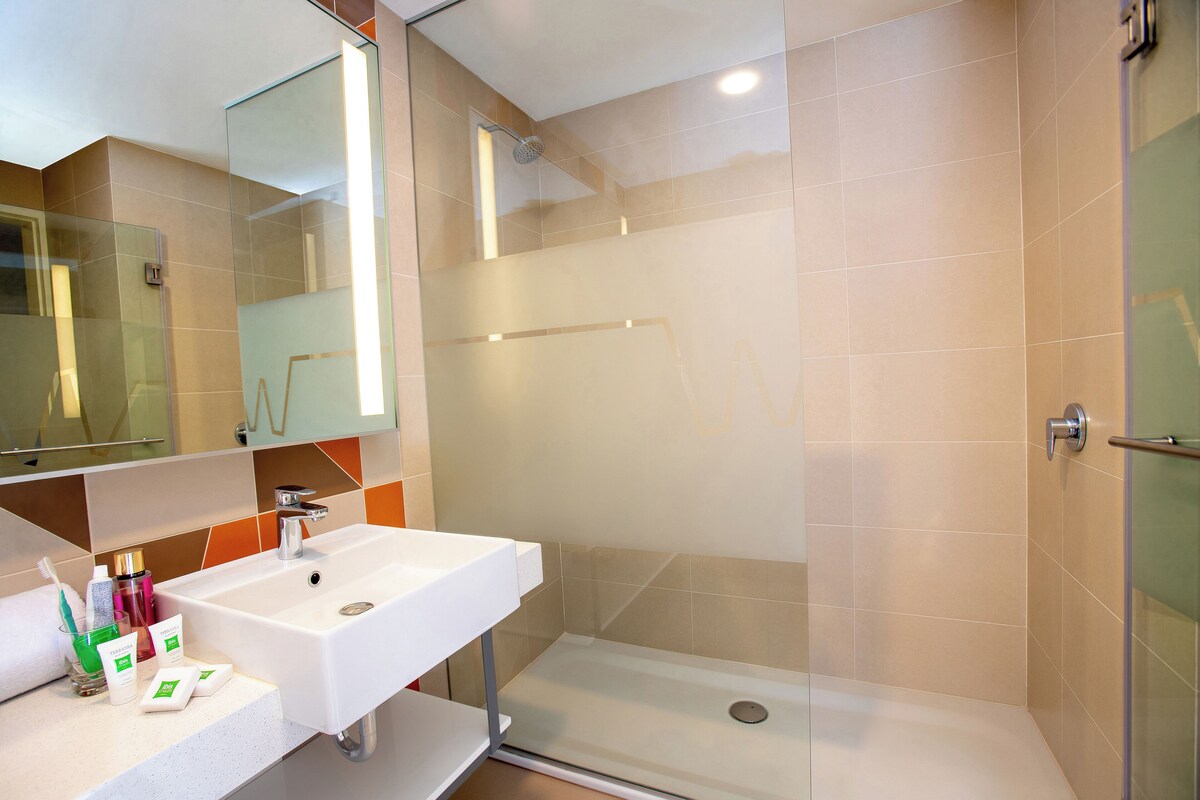 Une salle de bain moderne avec une douche à parois de verre, un lavabo blanc et un miroir au-dessus.