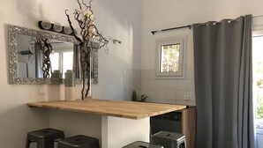 Keittiössä on puinen työtaso, kolme jakkaraa, peili ja ikkuna, jossa on verhot.