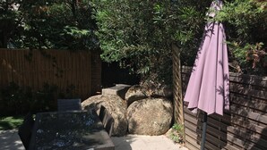 Ulkoterassi, jossa on pöytä ja tuoleja, puinen aita ja pergola, jonka yllä on violetti katos.