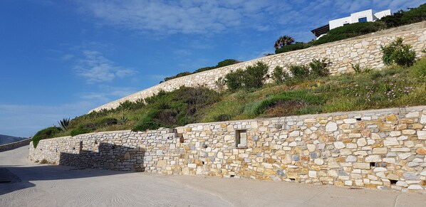 A stone retaining wall with a small window, a paved road, and a building in the background.